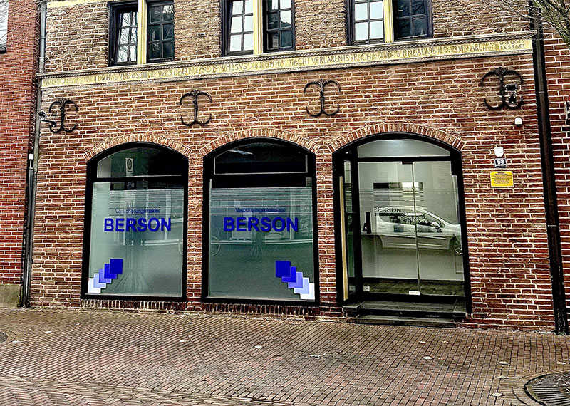 Straßenansicht der modernen Büroräume von Berson in Kranenburg, mit drei großen Fenstern in einer roten Backsteinfassade. Auf den Fenstern steht der Firmenname ‚BERSON‘ in blauer Schrift.