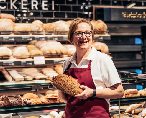 Fröhliche Mitarbeiterin einer Bäckerei mit Brot in der Hand
