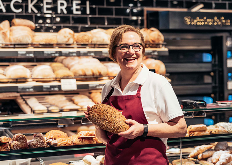 Fröhliche Mitarbeiterin einer Bäckerei mit Brot in der Hand