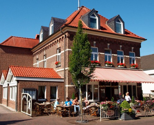 Außenansicht des Schnellrestaurants Peters Kranenburg bei schönem Wetter, einige Tische sind besetzt und eine Kellnerin bedient