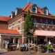 Außenansicht des Schnellrestaurants Peters Kranenburg bei schönem Wetter, einige Tische sind besetzt und eine Kellnerin bedient