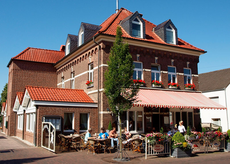 Außenansicht des Schnellrestaurants Peters Kranenburg bei schönem Wetter, einige Tische sind besetzt und eine Kellnerin bedient