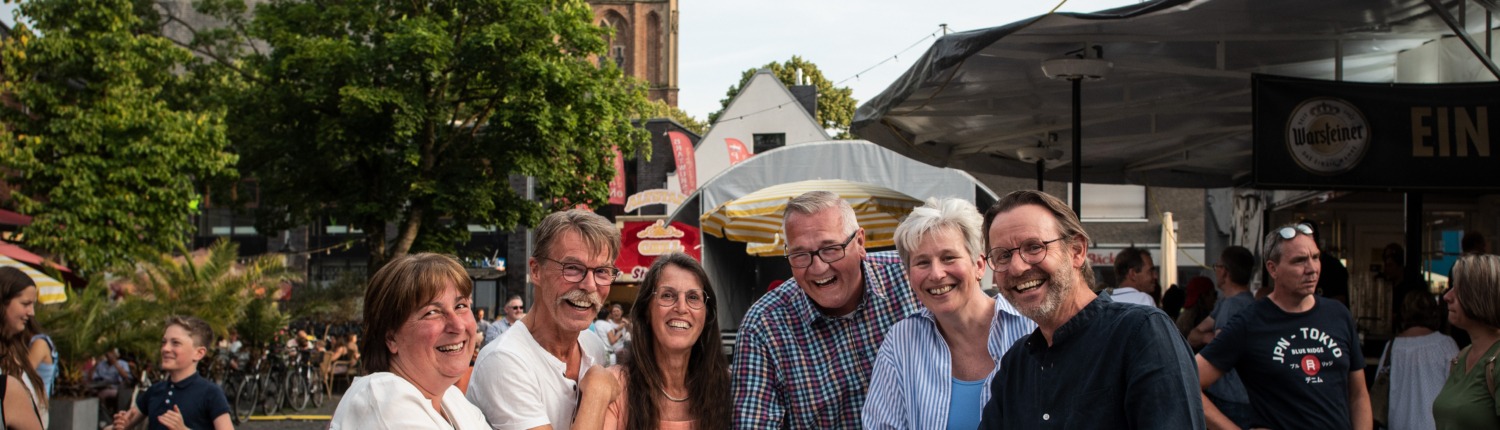 Personengruppe mit Getränken am Stehtisch auf dem Kranenburger Stüppkesmarkt im Vordergrund des Bildes, im Hintergrund des Bildes die Kranenburger Kirche (Foto: Markus van Offern/Gemeinde Kranenburg)