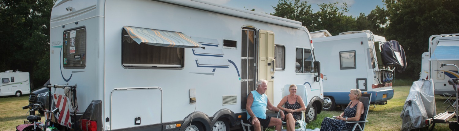 Wohnmobil mit drei fröhlichen Wohnmobilisten auf Stühlen davor, im Hintergrund stehen auch andere Wohnmobile (Foto: Gemeinde Kranenburg)